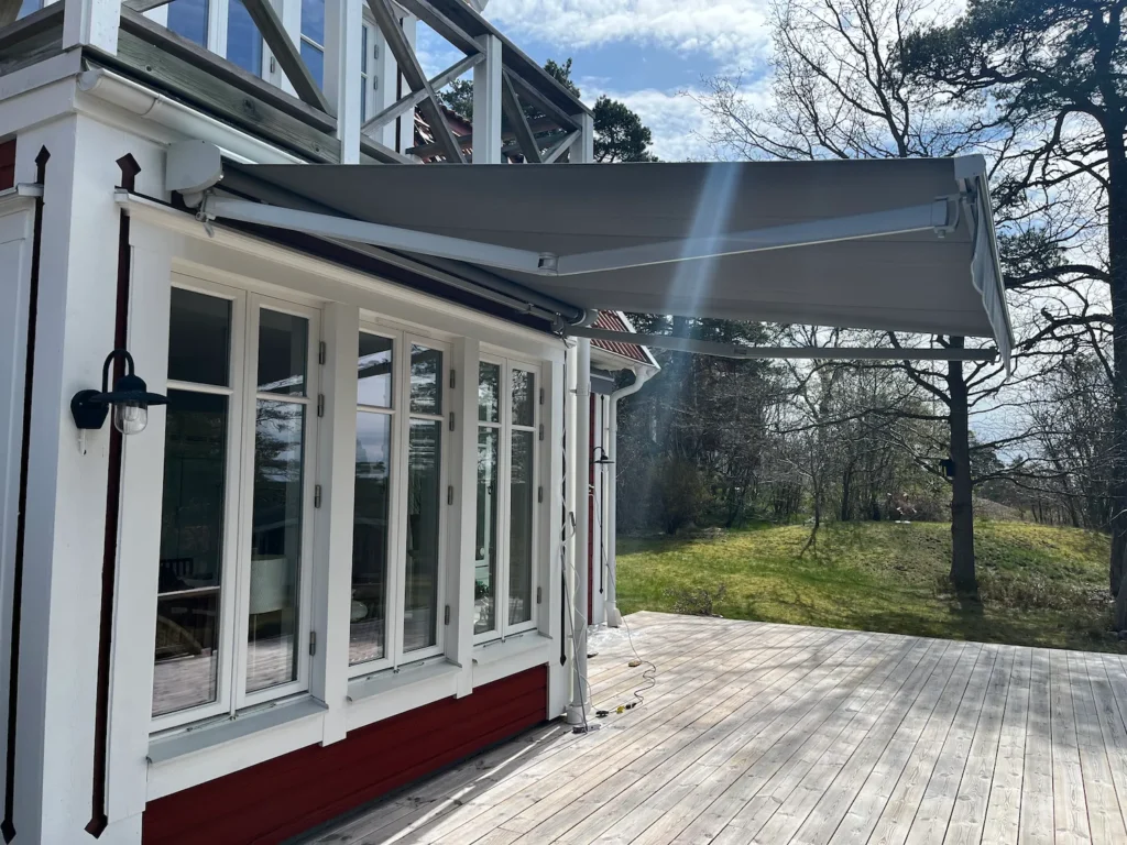Grå terassmarkis på rött hus med vita knutar